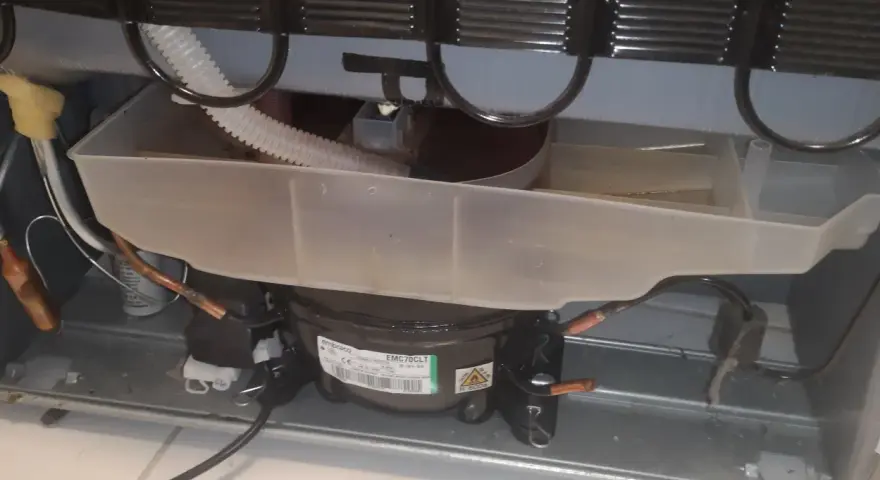 Widok wnętrza lodówki Whirlpool z widocznym kompresorem i tacą skraplacza.