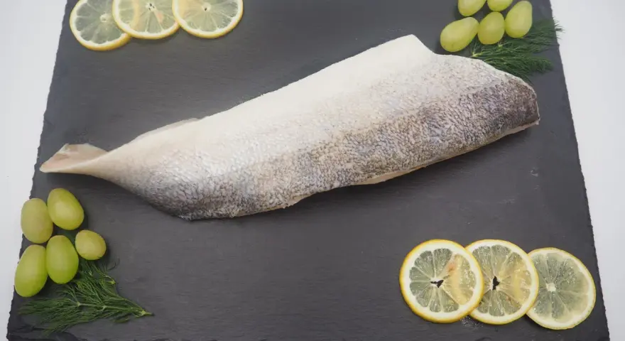 Filet ryby na czarnej desce z plasterkami cytryny, winogronami i koperkiem.